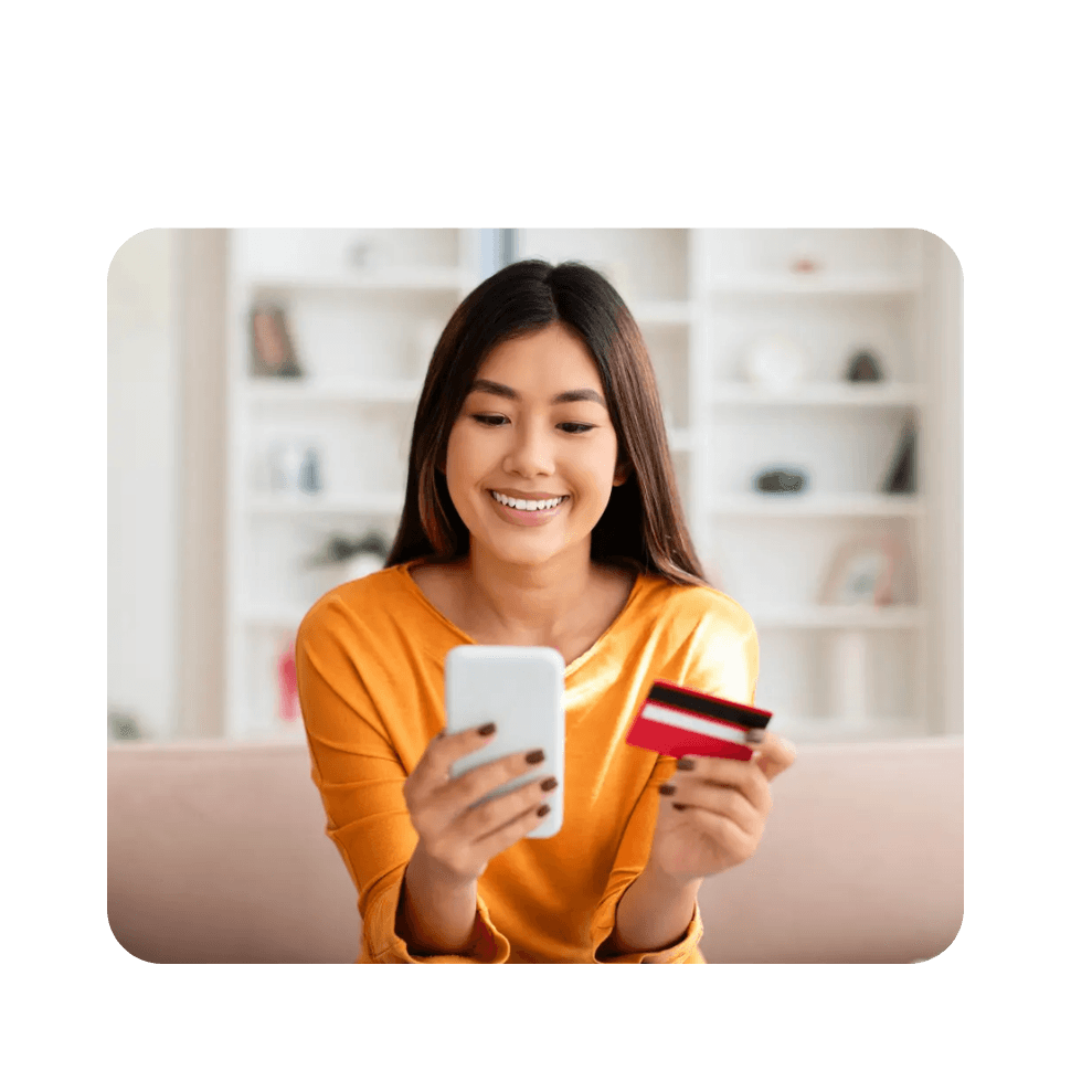 Woman in orange shirt smiling whilst holding smartphone and credit card for online shopping
